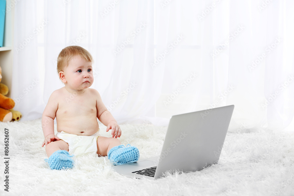 Cute baby boy sitting with laptop on carpet, on light background Cute baby boy sitting with laptop on carpet, on light background