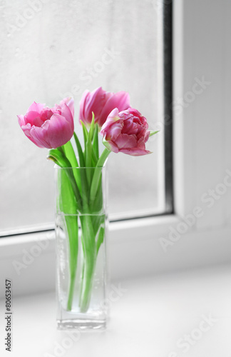 Beautiful pink tulips in vase on windowsill background