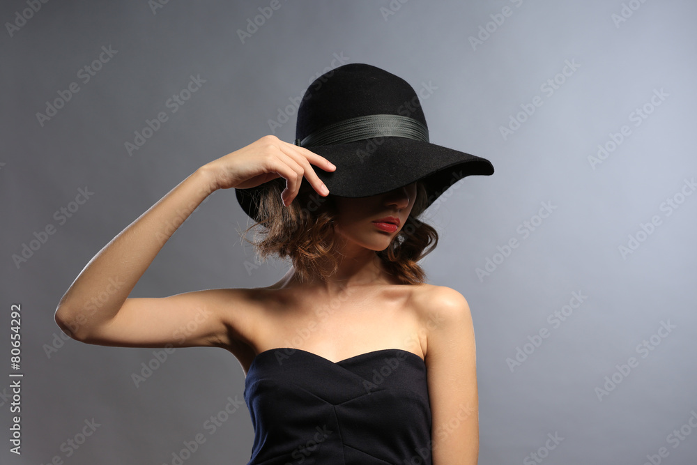 Portrait of beautiful model in black dress and hat on gray background Portrait of beautiful model in black dress and hat on gray background