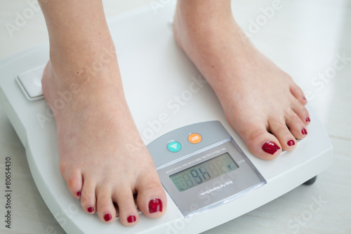 Mujer joven sobre una balanza midiendo su peso y porcentaje grasa corporal Fototapet