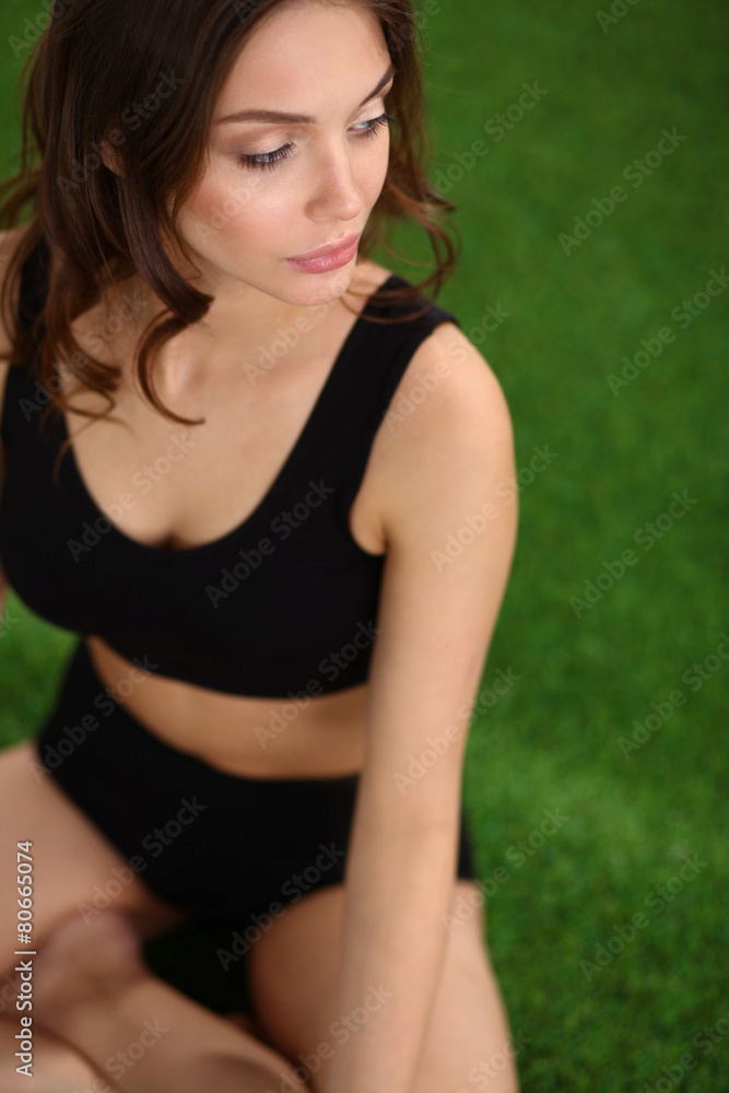 Fototapeta premium Young fitness girl sitting on green grass