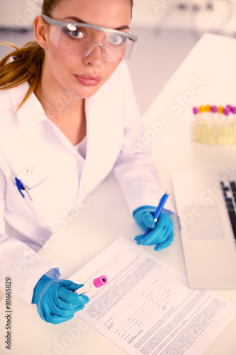 Woman researcher is surrounded by medical vials and flasks