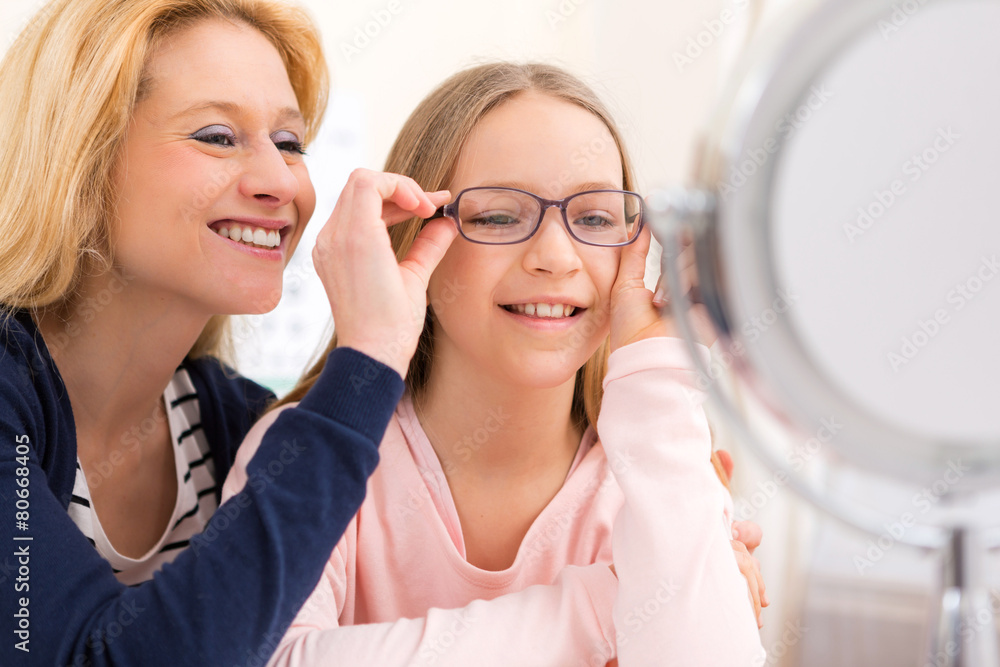 Young little girl trying glasses at the optician w her mother Young little girl trying glasses at the optician w her mother
