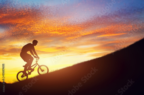 Obraz na plátně Man riding a bmx bike uphill against sunset sky. Challenge.