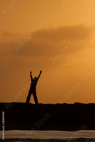 Hombre solitario haciendo un gesto de júbilo o recibiendo la energía del sol mientras camina sobre un espolón al lado del mar en un hermoso atardecer en Cartagena de Indias en Colombia