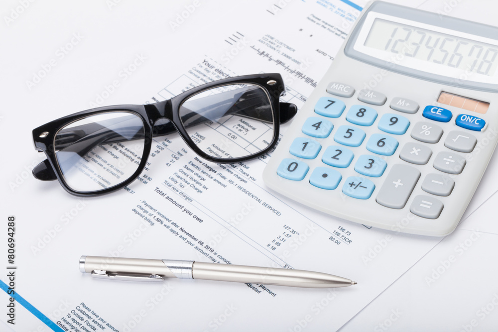 Calculator with pen, glasses and utility bill under it Calculator with pen, glasses and utility bill under it