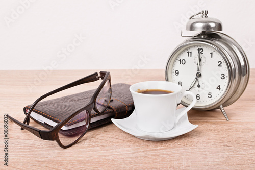 Glasses, notebook, alarm clock and coffee cup