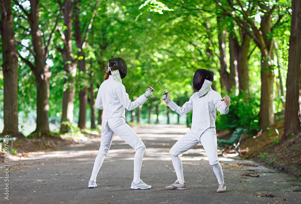 Two rapier fencers women staying in park alley getting ready for