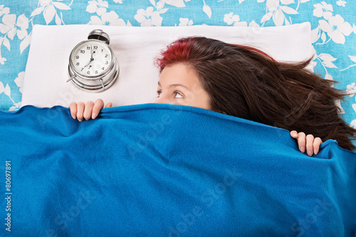 Young girl in bed hiding beneath her blanket from the alarm cloc photo