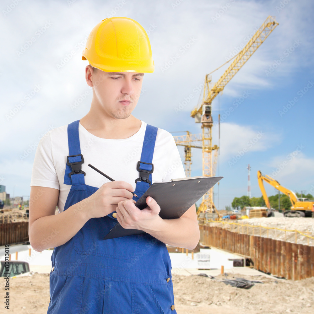 young handsome man in builder uniform with clipboard at constru young handsome man in builder uniform with clipboard at constru