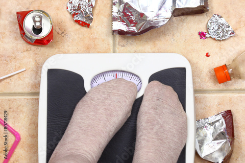 Feet on bathroom scale with junk food garbage around