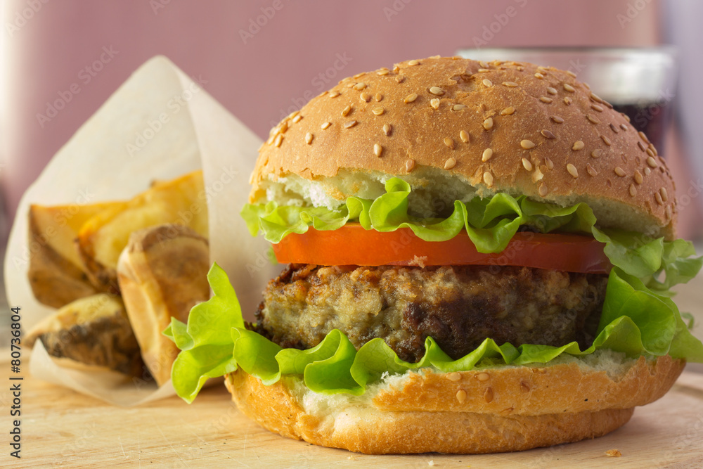Burger on wooden plate and roasted potato wedges Burger on wooden plate and roasted potato wedges