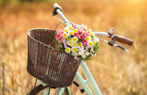 Vintage bicycle with basket full of flowers standing in field photo