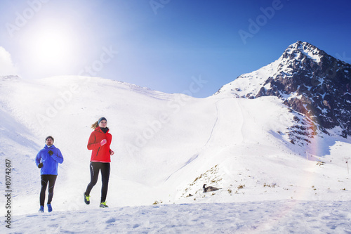 Young couple jogging outside in sunny winter mountains