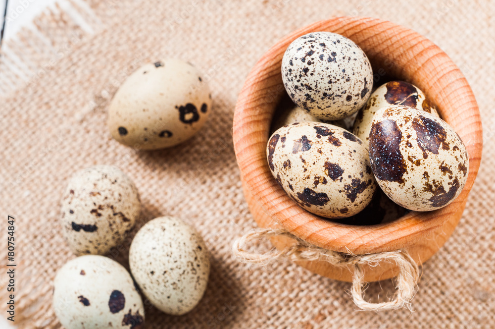Obraz premium raw quail eggs in a wooden bowl on burlap background