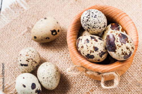raw quail eggs in a wooden bowl on burlap background