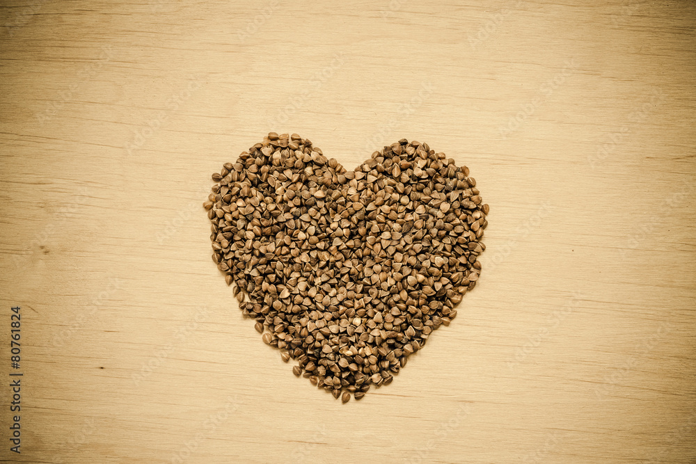 buckwheat groats heart shaped on wooden surface.