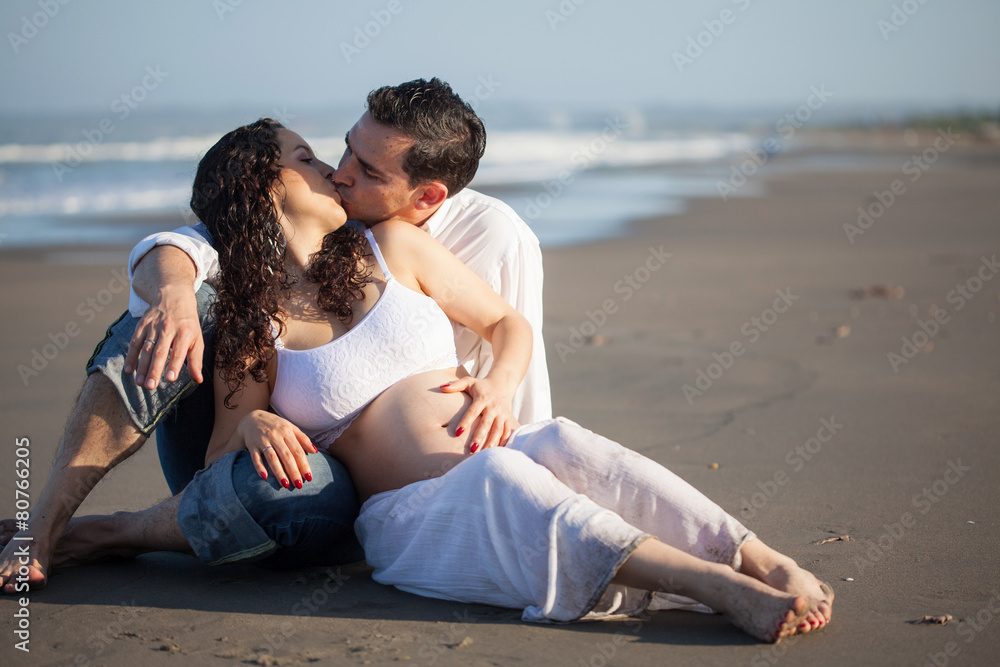 Mujer joven embarazada disfrutando de un hermoso día de sol con su esposo en la playa Mujer joven embarazada disfrutando de un hermoso día de sol con su esposo en la playa
