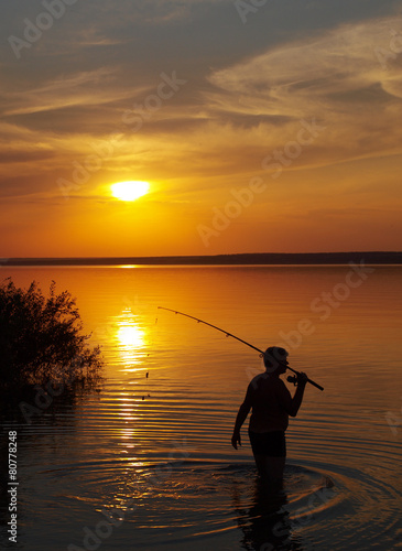 Fisherman catches fish by spinning on the lake at sunset © romensky