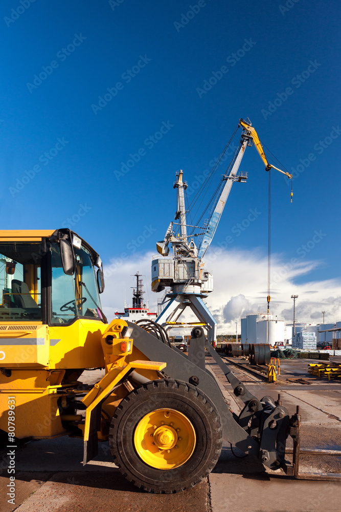 Yellow forklift and crane at loading and unloading of cargo in t Yellow forklift and crane at loading and unloading of cargo in t