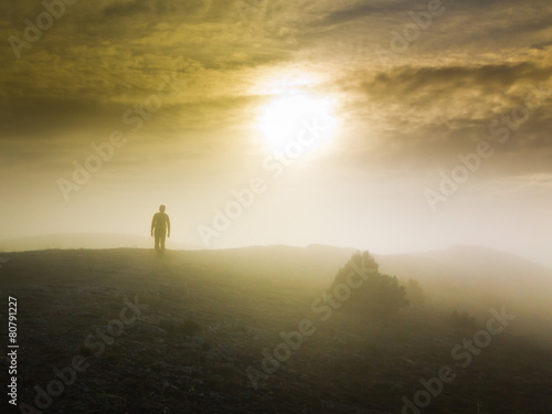 man walking over a hill in foggy weather at sunset