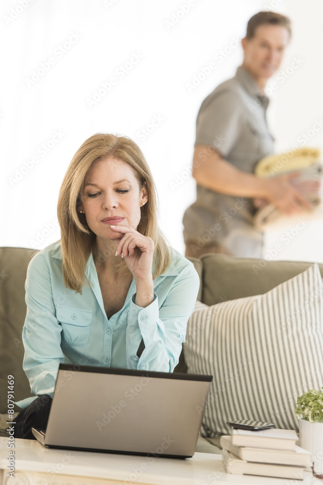 Mature Woman Using Laptop While Man In Background At Home Mature Woman Using Laptop While Man In Background At Home
