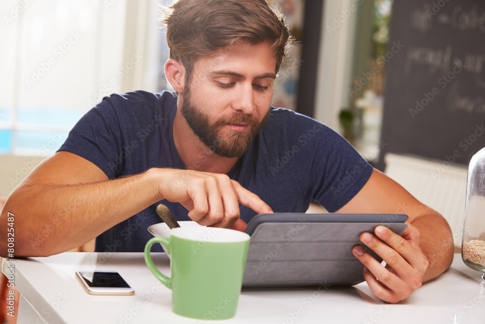 Young Man Eating Breakfast Whilst Using Digital Tablet Young Man Eating Breakfast Whilst Using Digital Tablet