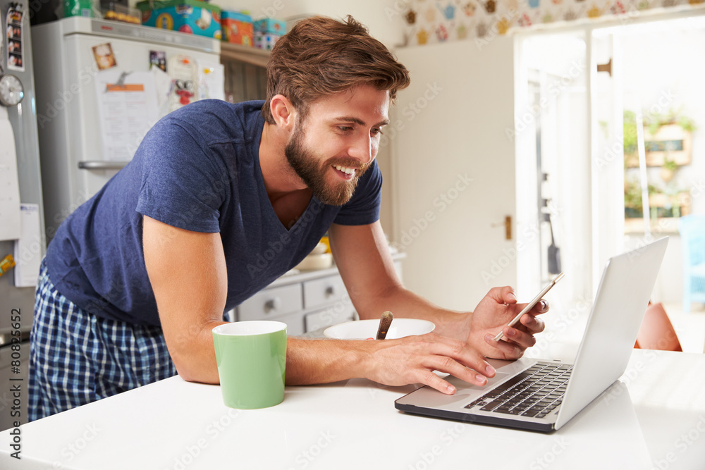 Man Eating Breakfast Whilst Using Mobile Phone And Laptop
