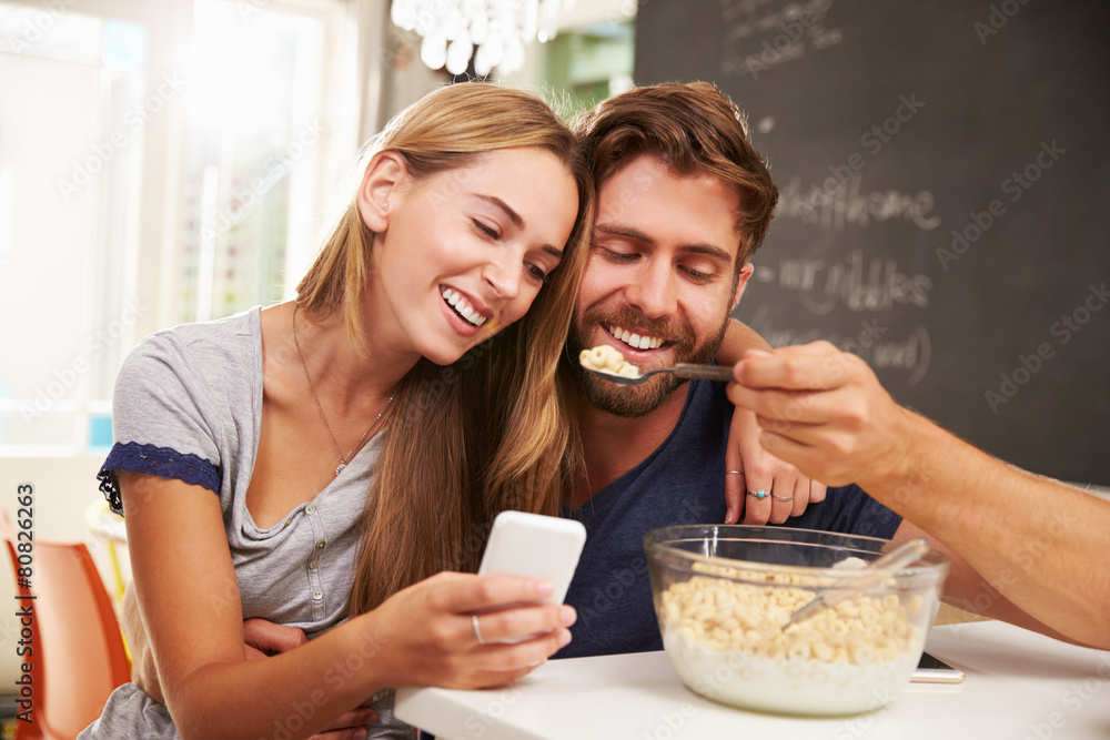 Young Couple Eating Breakfast Whilst Using Mobile Phones Young Couple Eating Breakfast Whilst Using Mobile Phones