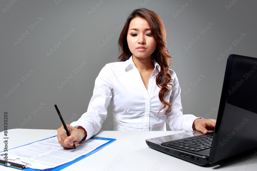Young businesswoman writing while working with a laptop Young businesswoman writing while working with a laptop