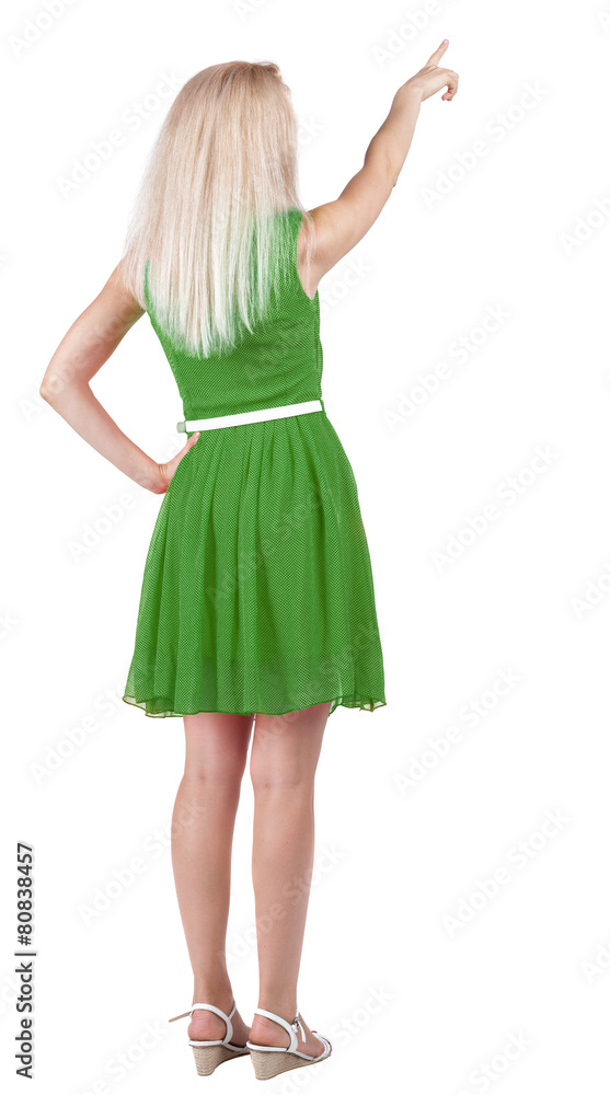 Back view of young blonde woman pointing at wall.