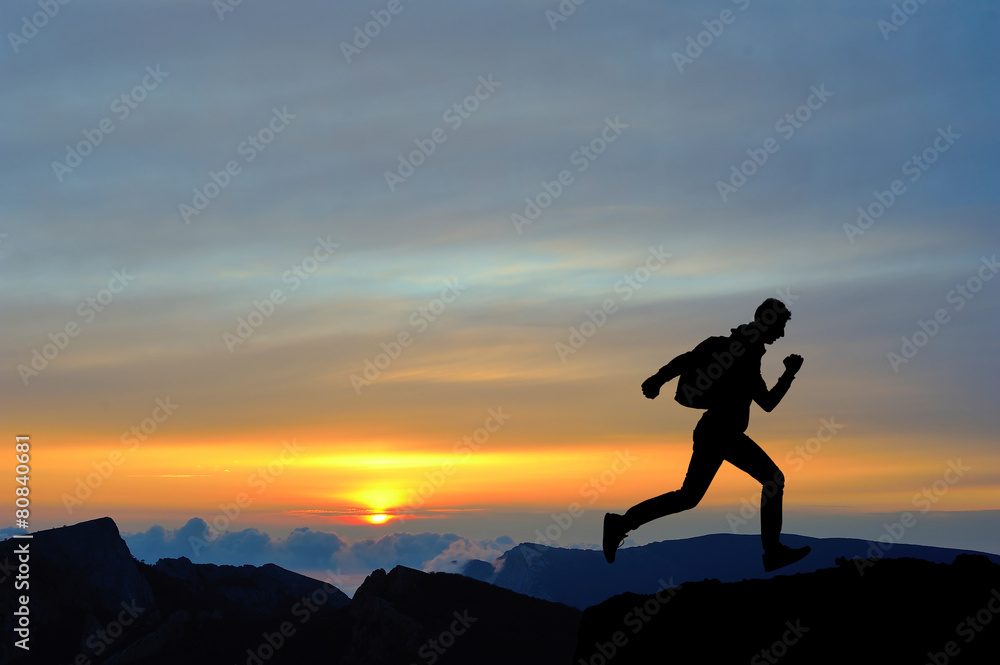 Running jumping man above sunset and mountain. Sport sky
