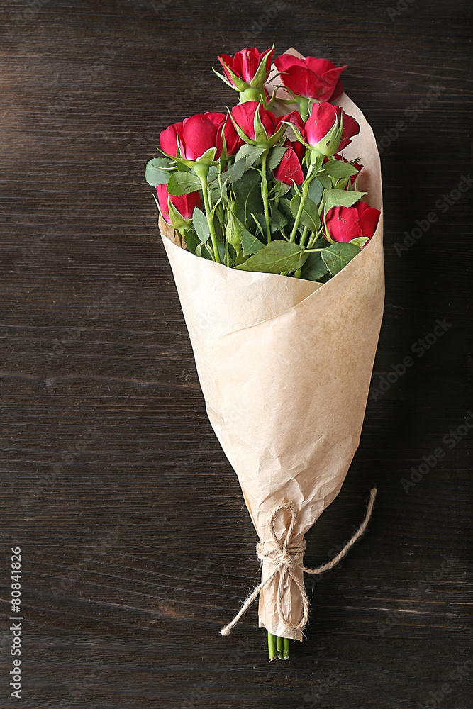 Obraz premium Red roses wrapped in paper on wooden table background
