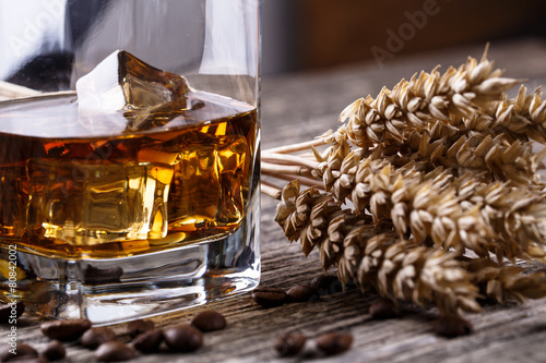 Canvas Print Glass of whiskey with ice and wheat on a wooden table.