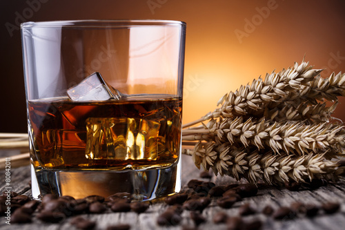 Glass of whiskey with ice and wheat on a wooden table.