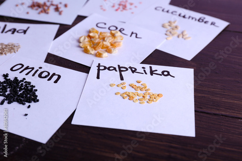 Different seeds on pieces of paper on wooden background © Africa Studio