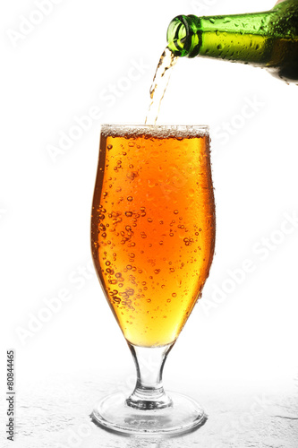 Pouring beer from bottle into glass isolated on white