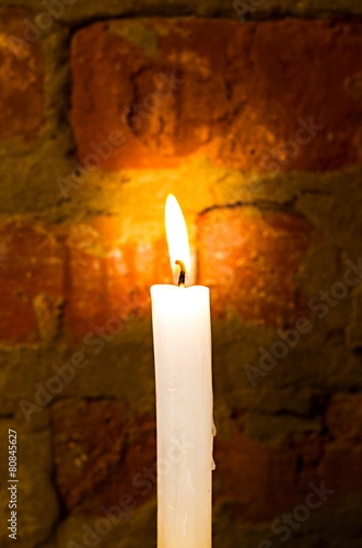 Burning candle on a background of a brick wall