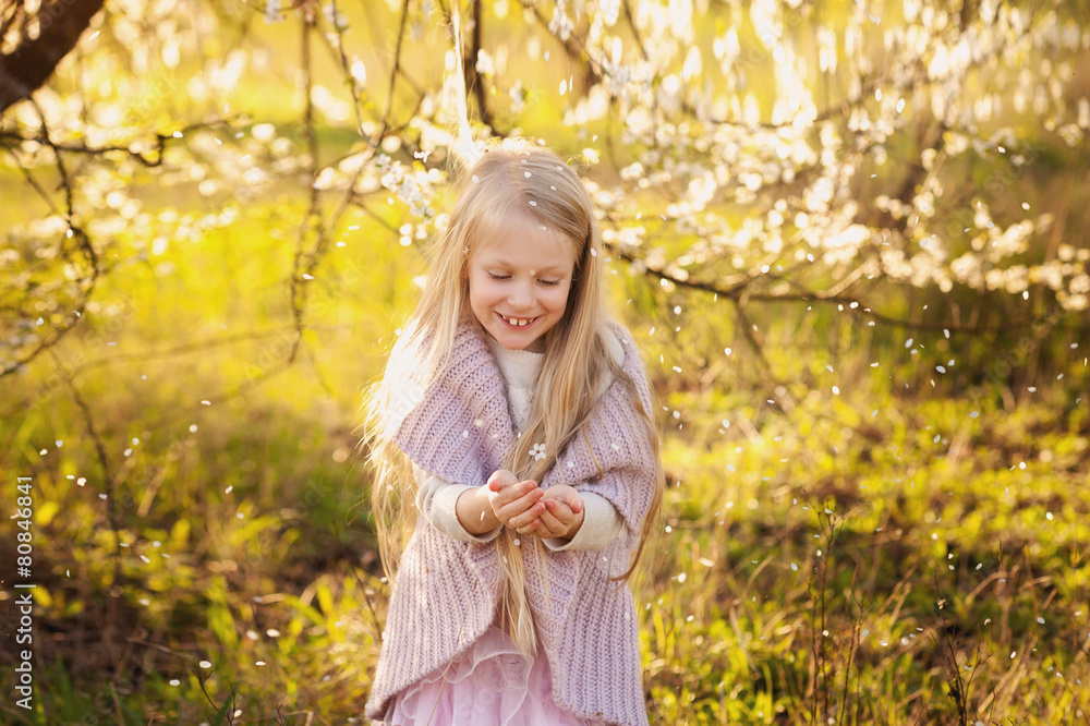 Little blond girl in the lush spring garden plays Little blond girl in the lush spring garden plays