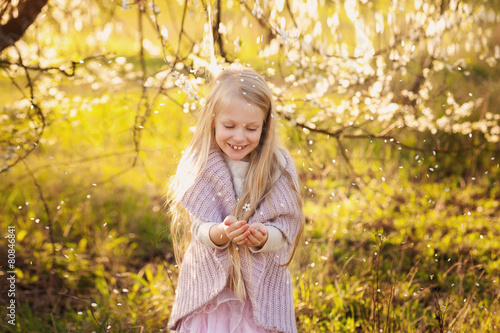 Little blond girl in the lush spring garden plays