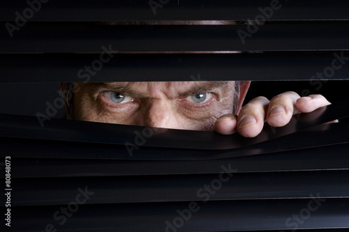 Man spying on something through venetian blinds photo