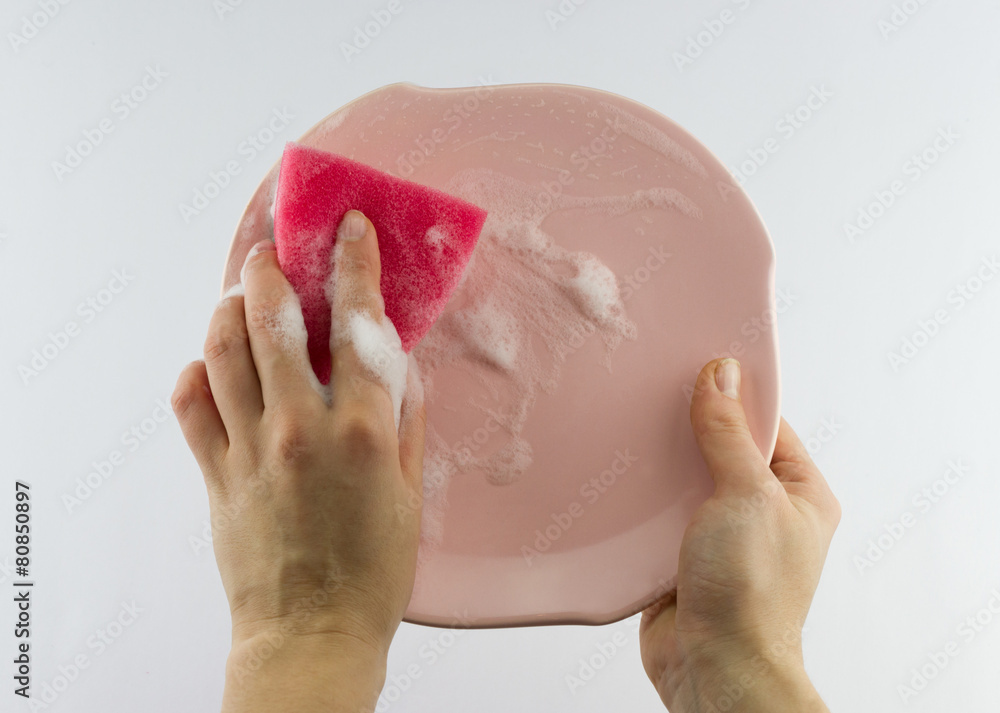 Fototapeta premium Female hand with red sponge washing pink plate 