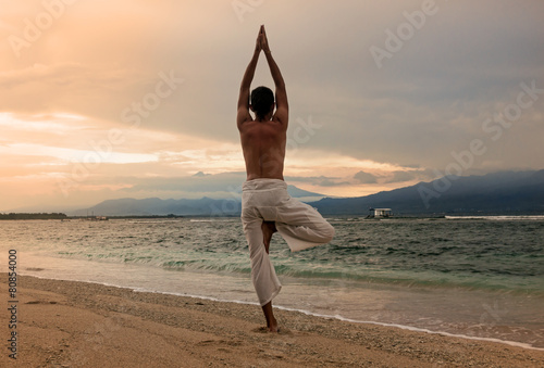 Man doing yoga on the sand beach with sunset