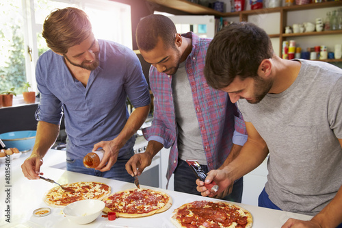 Three Male Friends Making Pizza In Kitchen Together © Monkey Business