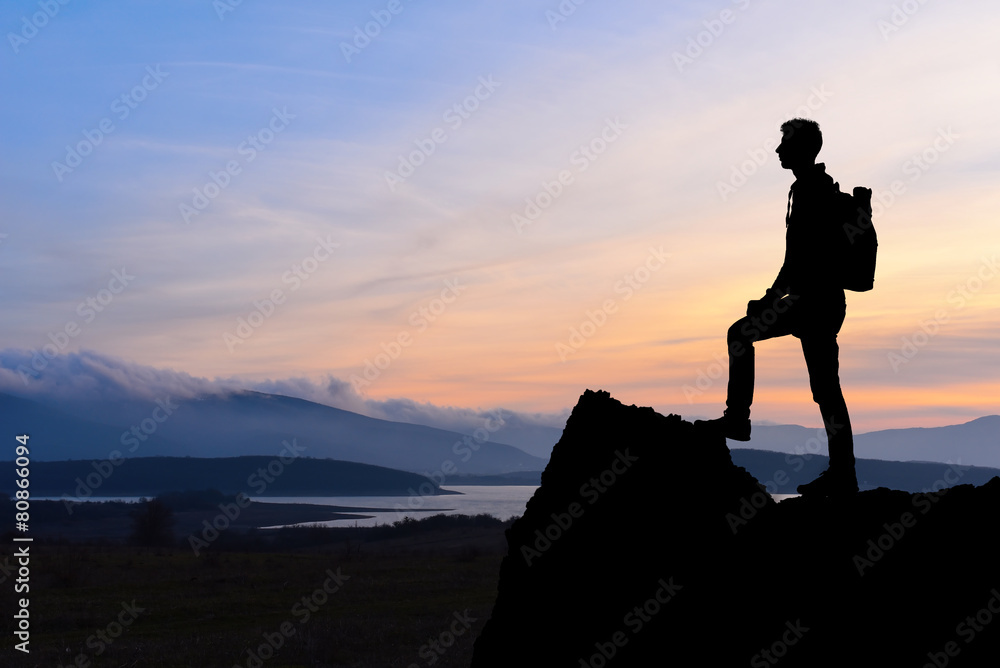 Silhouette of man at the top of the mountain on sunset.