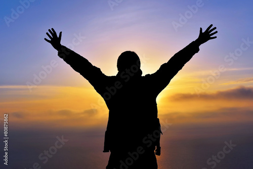 Young man standing with arms outstretched at sunset