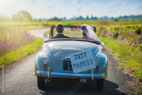 A newlywed couple is driving a retro car, rear view photo