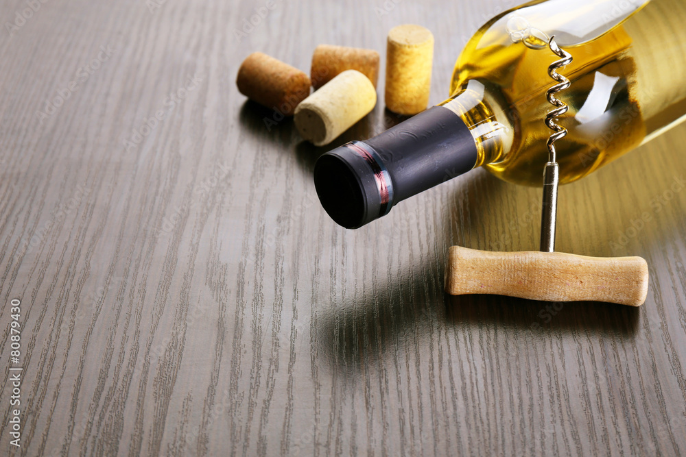 Bottle of wine with corks and corkscrew on wooden background