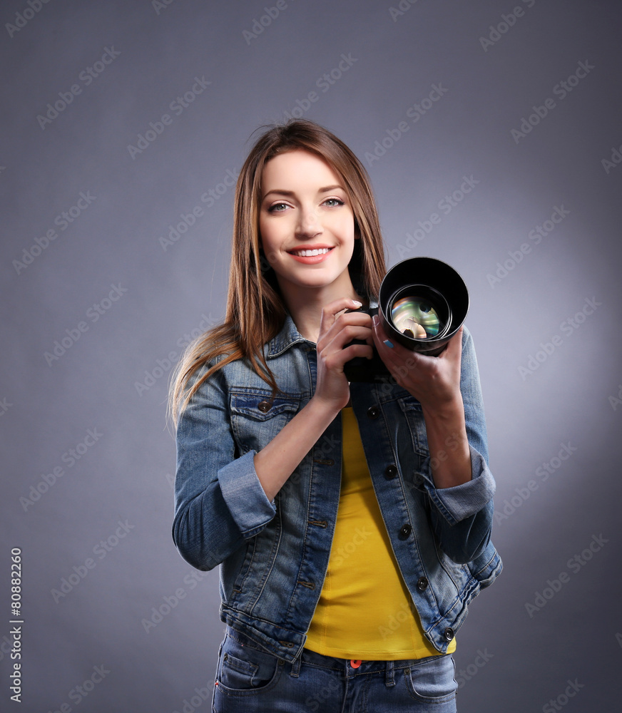 Obraz premium Young female photographer taking photos on grey background