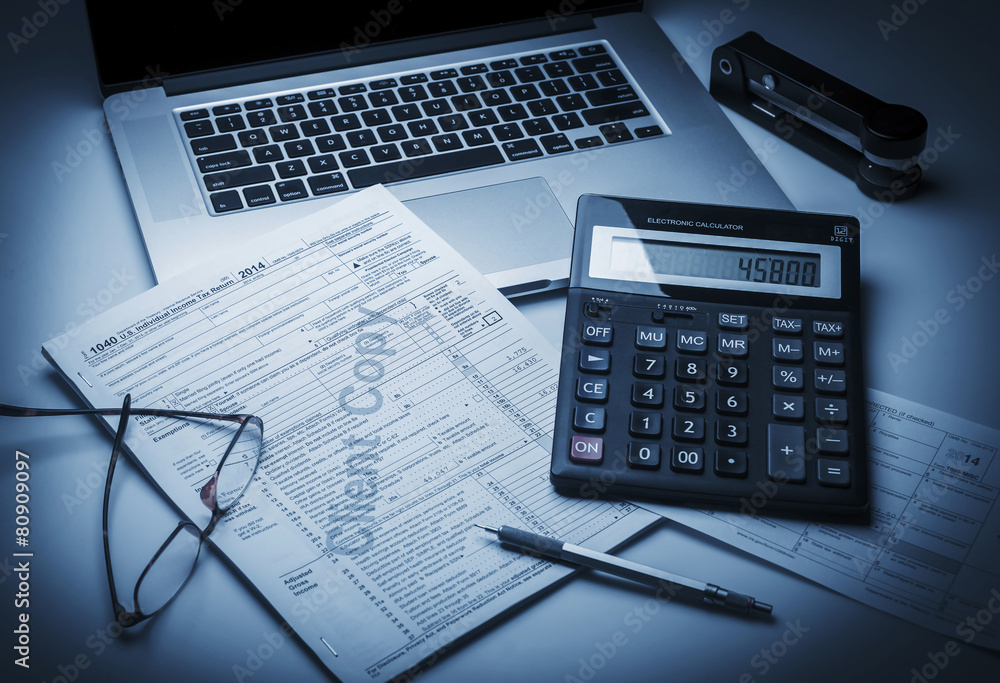 Preparing 1040 US Tax Form, with laptop, calculator and pen Preparing 1040 US Tax Form, with laptop, calculator and pen